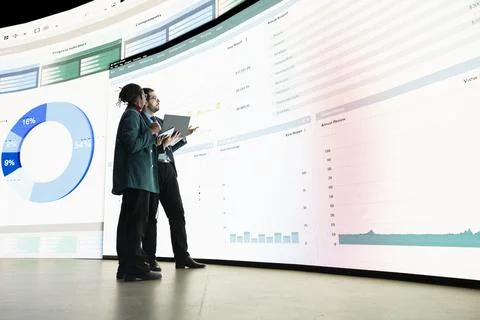 Calculating expenses, graph displayed on videowall and team of investors Stock Photos