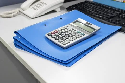 Calculator with blue folder on table in work office Fotos Stock