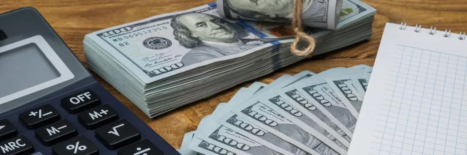 A calculator, dollars in a bundle, a roll and a fan, a notebook and a pen lie Stock Photos