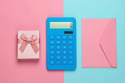 Calculator with envelope and gift box on pink-blue pastel background. Top vie 库存照片