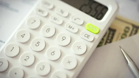 A calculator rests among business documents and cash on a cluttered office d Stock Footage 338187732
