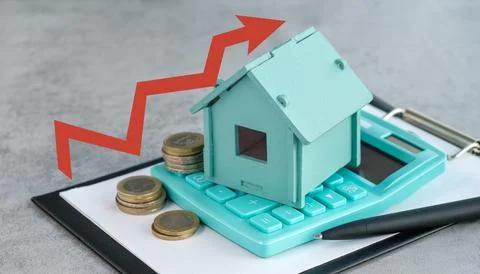 A calculator sits on top of a stack of coins and a house model Stock-Fotos