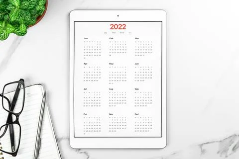 Calendar 2022. Tablet computer with open app. White marble background, busine Stock Photos