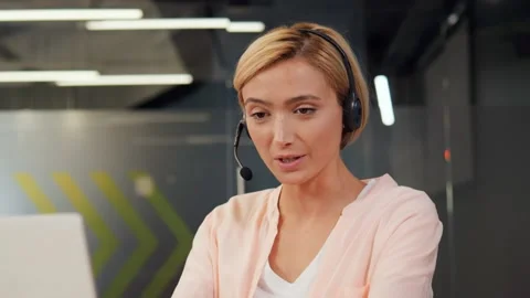 Call center agent providing support to customers via headset using her laptop. Video stock 238000024