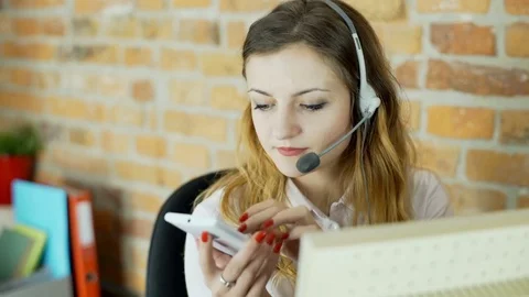 Call center agent sitting in the office and browsing internet on smartphone Видео 70432782
