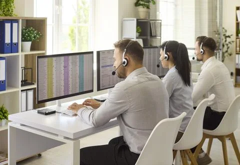 Call center agents with headsets working at computers in modern open office Stock Photos