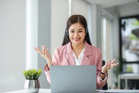 A call center operator is explaining job details to a customer on a laptop. Stock Photos