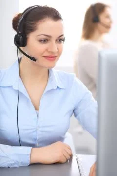Call center operator in headset. Young businesswoman sitting at desk and while Stockfoto's