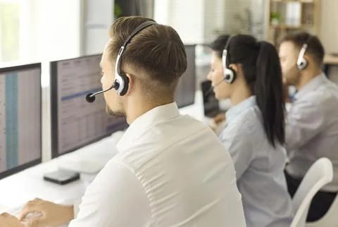 Call center operators with headsets working at computers in a modern office Stock Photos