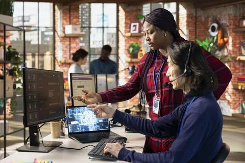 Call center supervisor guiding intern on how to use AI chatbot app on computer Stock Photos
