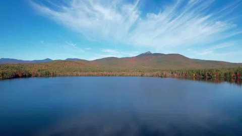 Calm autumn lake mirroring a pointed mountain peak, filmed from above Видео 348709853