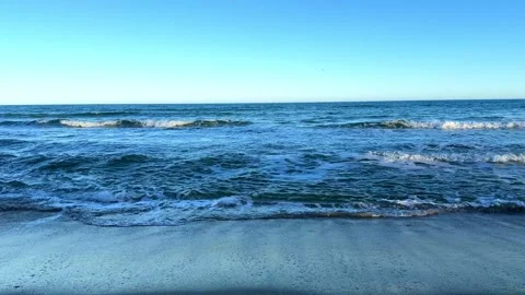 Calm blue ocean waves crashing on a sandy beach under a clear sunny sky Vídeos de archivo 335041008