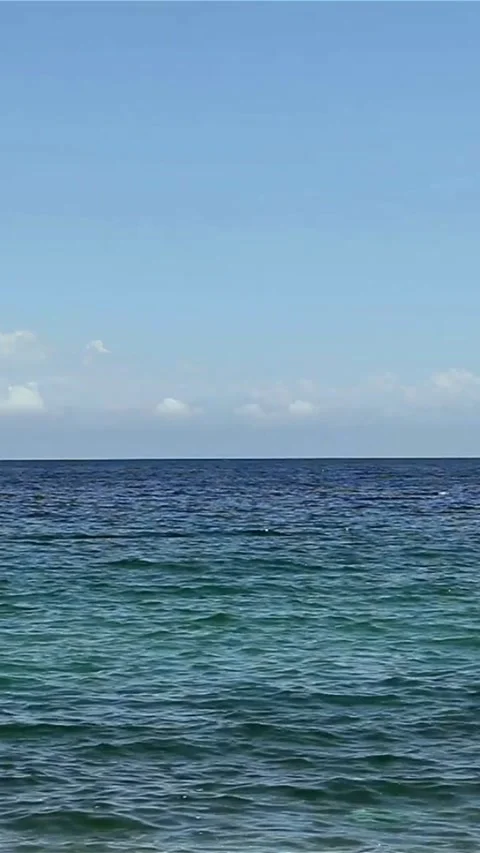 Calm blue ocean waves rolling under bright blue sky Stock Footage 334182181