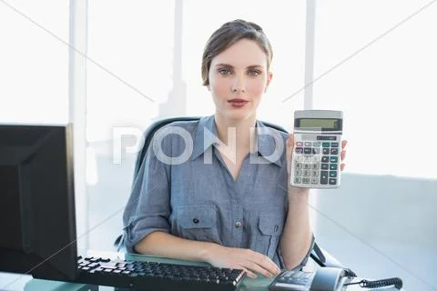 Calm businesswoman showing calculator sitting at her desk Stock Photos