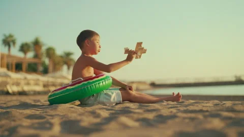 Calm child resting on beach in summer, playing with toy plane, weekend trip Stock Footage 317602900