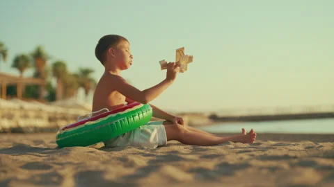 Calm child resting on beach in summer, playing with toy plane, weekend trip Stock Footage 317897947