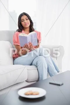 Calm cute brunette sitting on couch reading Stock Photos
