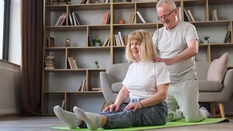 Calm elderly couple sitting on the floor at home, doing yoga. Grandfather gives Stock-Footage 252685361