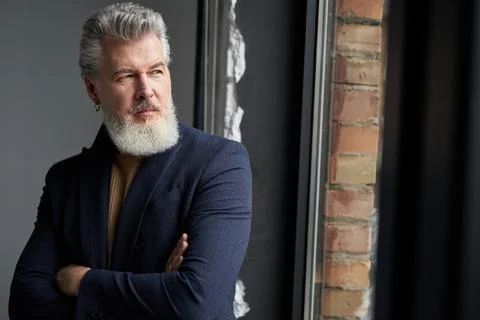 Calm gray haired middle aged man in business casual wear looking out a window Stock Photos