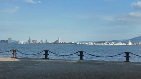 Calm harbor with small waves and a distant city skyline under a clear sky. 스톡 동영상 337277284