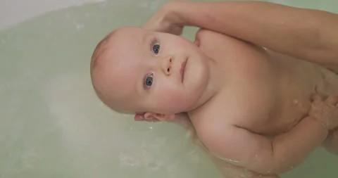 Calm infant lying in a bath and looking up with smile while mother washing him Vidéo 147217516