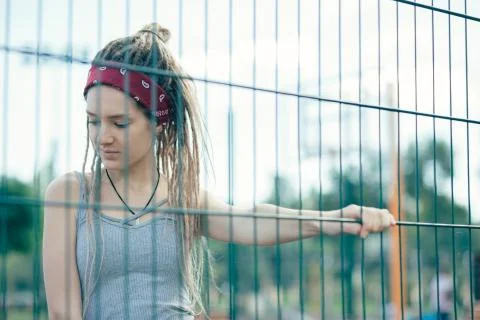 Calm lady thoughtfully looking down and touching the chain link fence Stock Photos