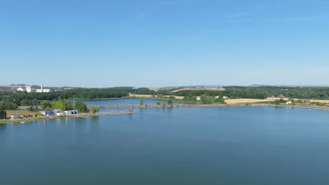A calm lake bordered by green trees, small buildings, and scattered houses on Stock Footage 346706179