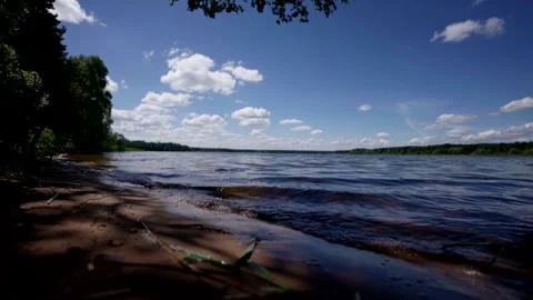 A calm lake with a dense forest around, under a light blue sky. The shadows of Stock Footage 280692776
