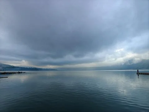 Calm Lake Landscape under Dramatic Overcast Storm Clouds with Mountains and Pier Stock Photos