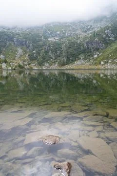 Calm lake in mountains with clear water, with reflection of rocky mountains on s Stock Photos