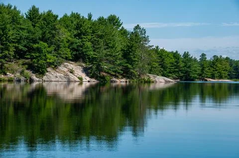 Calm Lake Reflection with Pine Trees &amp;amp; Rocky Shoreline on a Clear Summer Day Stock Photos