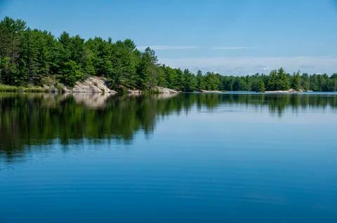Calm Lake Reflection with Pine Trees &amp;amp; Rocky Shoreline on a Clear Summer Day Stock Photos