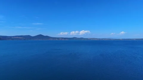 Calm lake surface reflecting blue sky with mountains in background Stock Footage 283308926