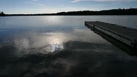Calm large lake with sun reflecting in the water, a dock along the right side  Stock Footage 219636503