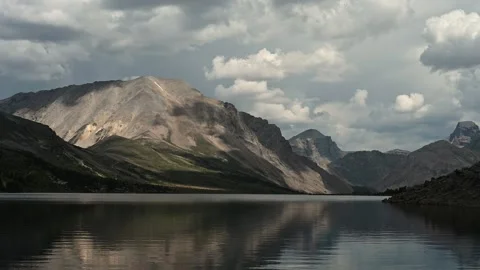 Calm large mountain lake reflects the surrounding mountains and the cloudy sky Stock Footage 289548204