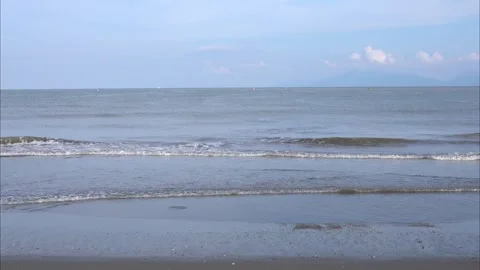 Calm light-blue ocean waves, crashing against empty and sandy beach Stock Footage 301944100