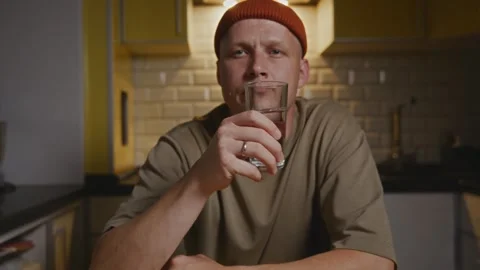 Calm man sitting in kitchen pausing during daily water ritual Stock Footage 317554194