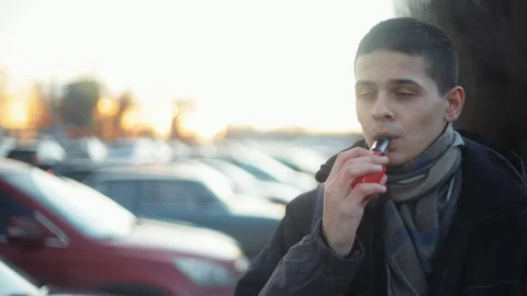 Calm man vaping e-cigarette between  cars on the parking zone near the mall, Stock Footage 121483028