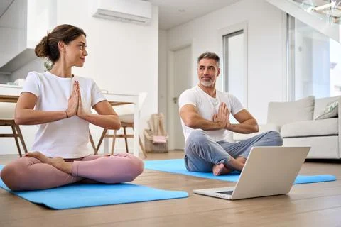 Calm middle aged couple learning online yoga meditating using laptop at home. Foto stock