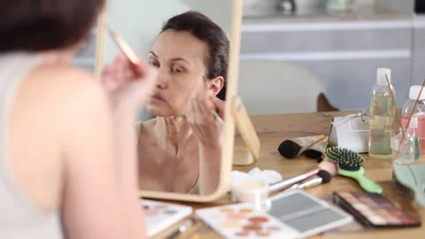 Calm middle-aged woman doing eyebrow make-up looking in the mirror while seated Stock Footage 306664606