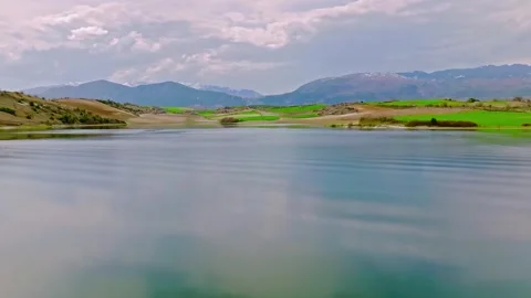 Calm mountain lake reflecting cloudy sky and green hills Stock Footage 345078507