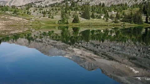 Calm mountain lake reflects the surrounding hills and trees while fish ripple th Stock Footage 289548308