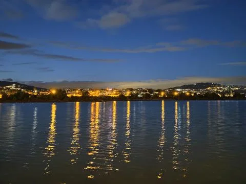 Calm nighttime waters mirror distant buildings and soft blue sky with spark.. Фото