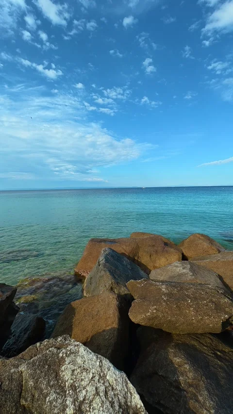 Calm ocean meets rugged rocks under vast blue sky. Nikiti, Greece. Vertical Video stock 339025700