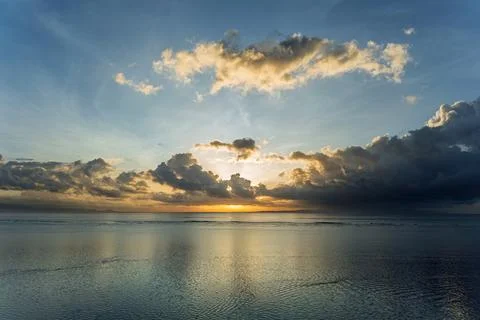 Calm ocean at sunset glows under dramatic storm clouds, wide horizon with g.. Stock Photos