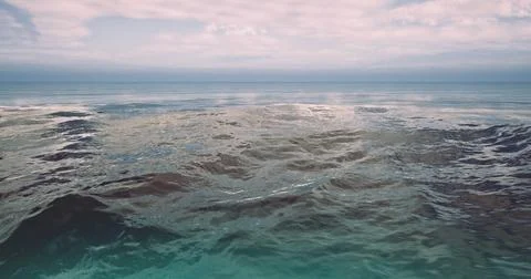 Calm ocean waters beneath a clear sky with gentle waves at sunset Ilustración de archivo