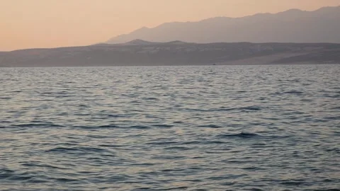 Calm ocean waters stretch toward distant hazy mountains at dusk. Stock Footage 337407500