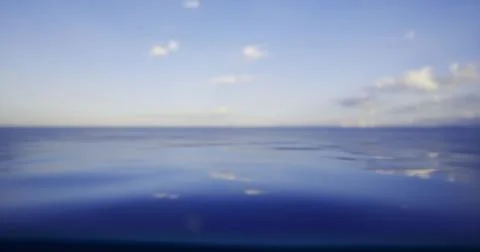 Calm ocean waters under a clear blue sky with scattered clouds at sunset 스톡 일러스트
