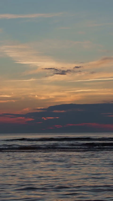 Calm ocean waves beneath glowing sunset clouds over open horizon, with soft Stock Footage 345125681