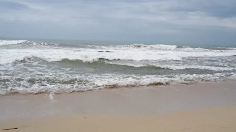 Calm ocean waves breaking on a sandy shore under a cloudy sky. Stock Footage 329782998